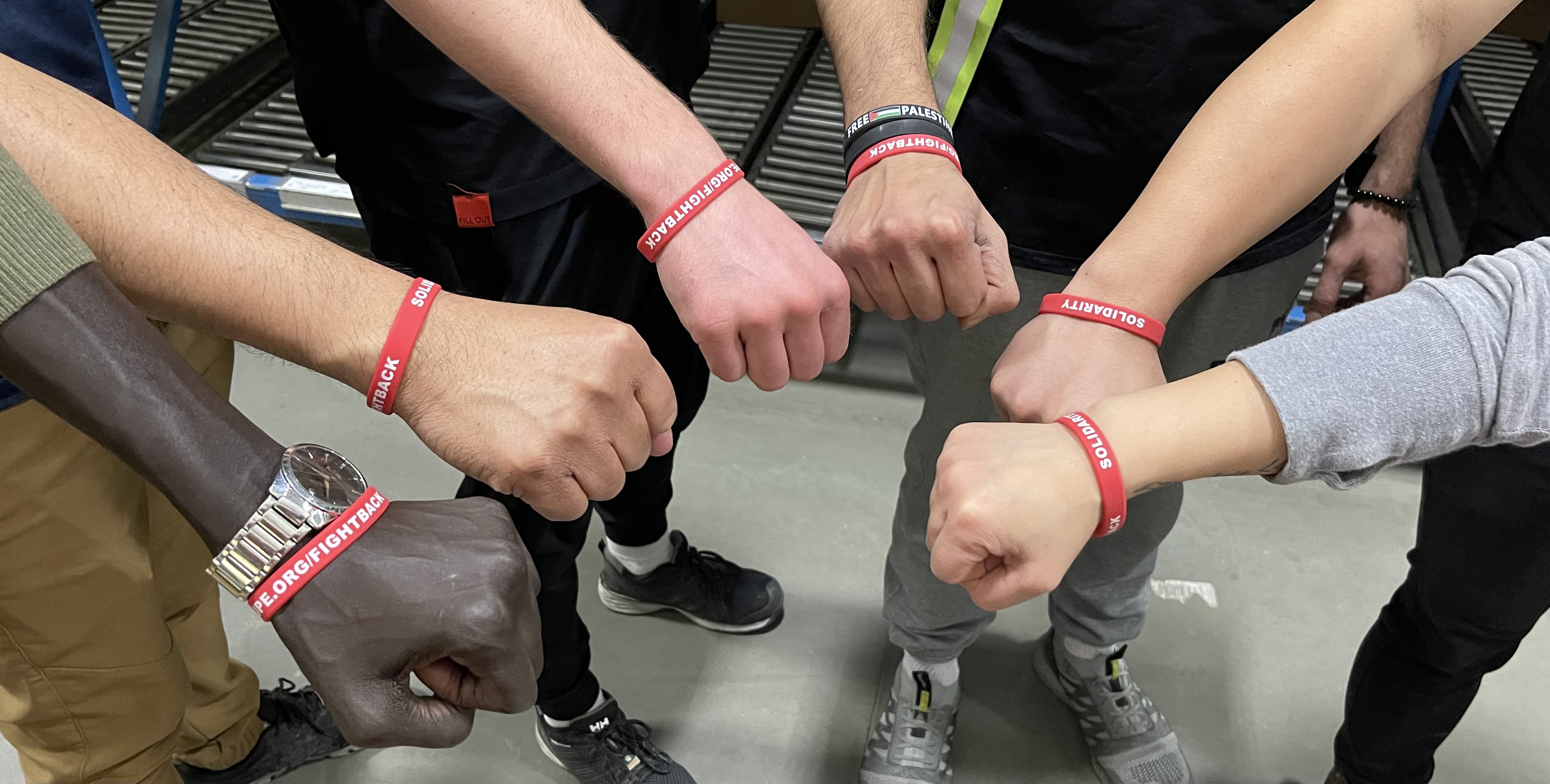 Members wearing red AUPE wristbands make a circle with their fists.