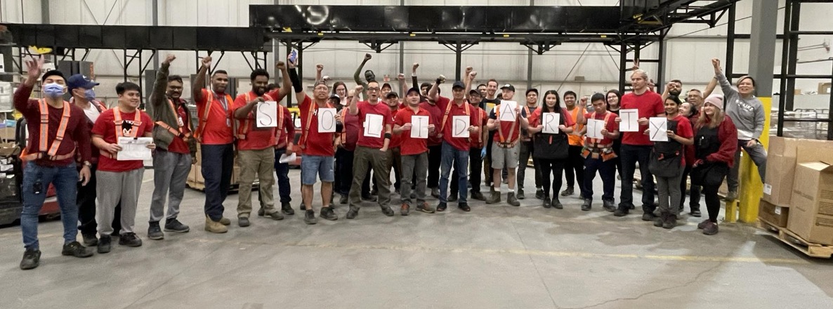 AUPE members pose with their red shirts and raised fists in a warehouse.