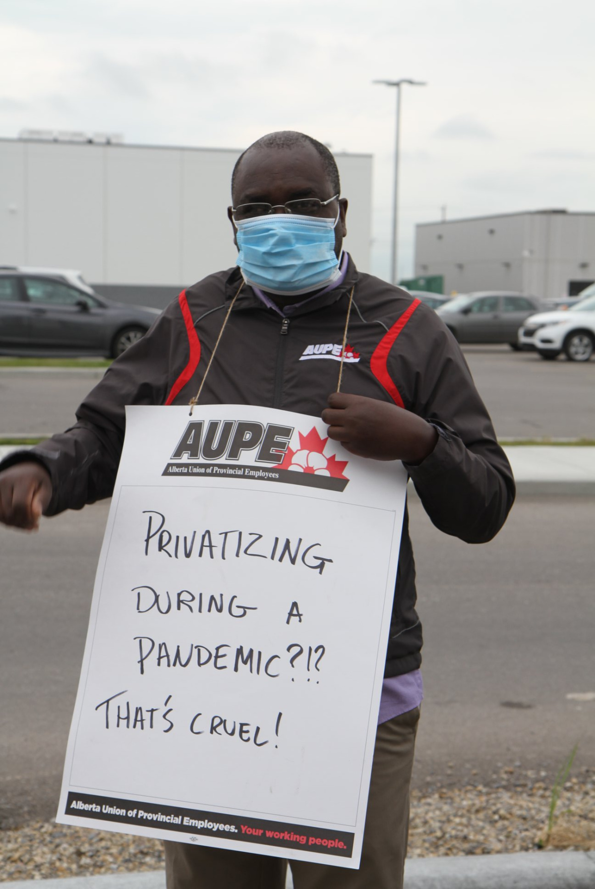 Member in face mask with sign that reads Privatizing during a pandemic?!? That's cruel.