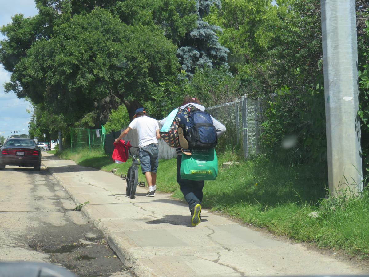 two homeless community members, Andre and Mary, walk down the street with their belongings