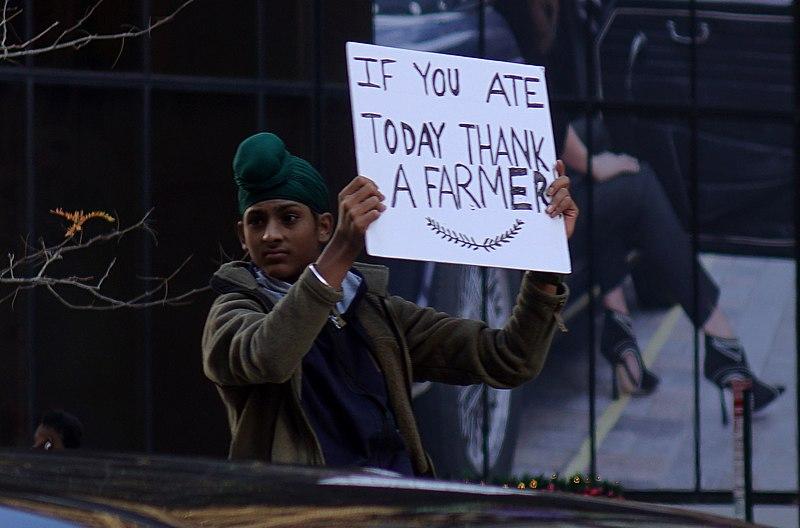 A young Sikh boy holds up a sign at a protest. The sign reads &quot;if you ate today, thank a farmer.&quot;