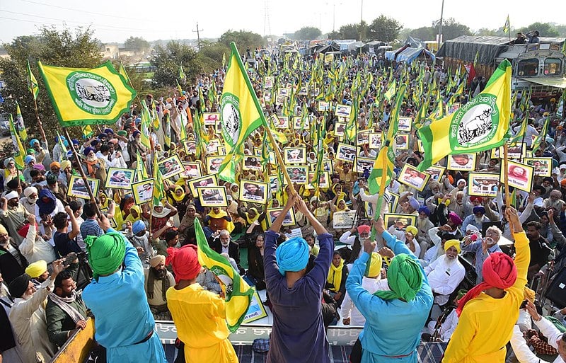 Protesters raise their fists in defiance as a crowd of protesters, many carrying farmer flags, cheers