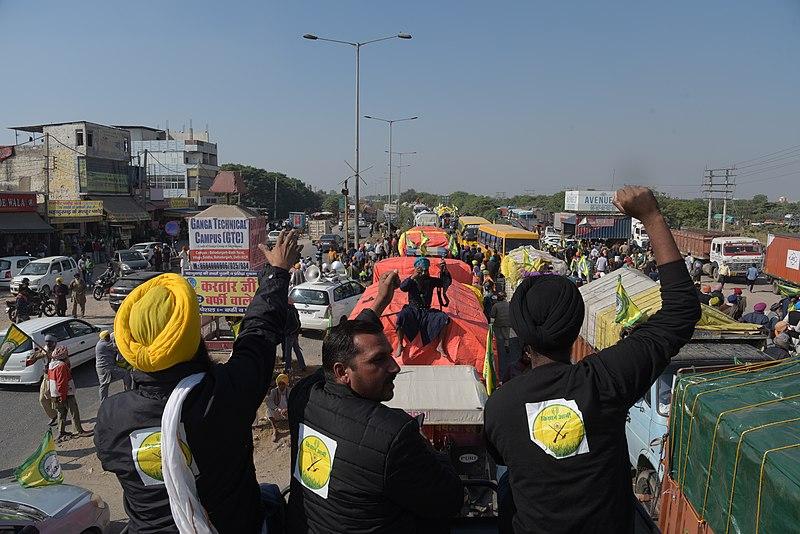 Protesters sit in the back of a farm vehicle, and cheer on a convoy of other protesters in vehicles as they block a road in India