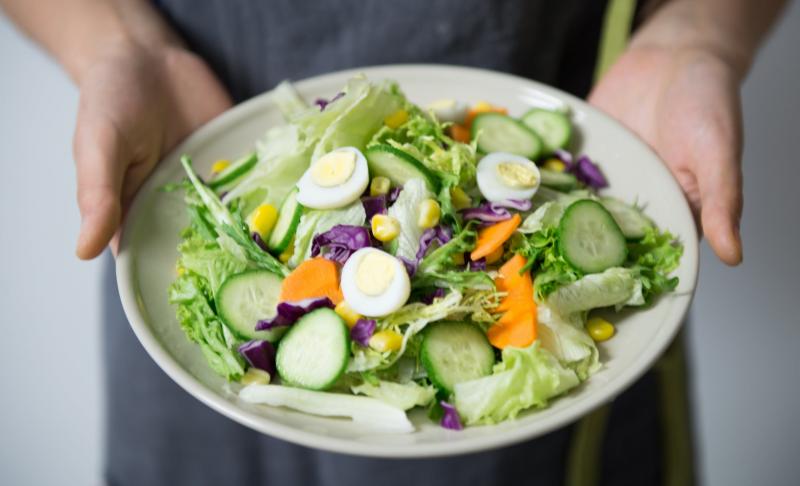 A person holds up a plate with a fresh salad on it, as if to serve it to the viewer.