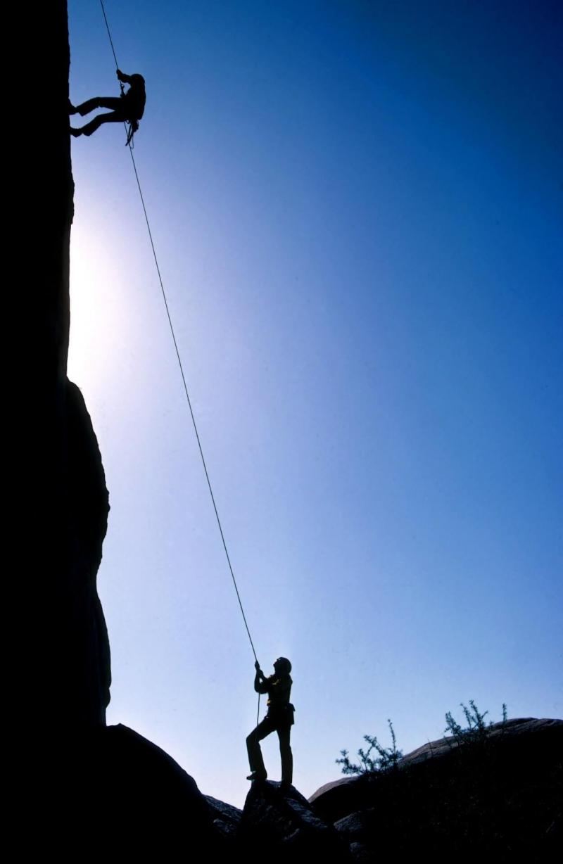 A rock climber is spotted by their partner. Only their silhouettes are visible. 